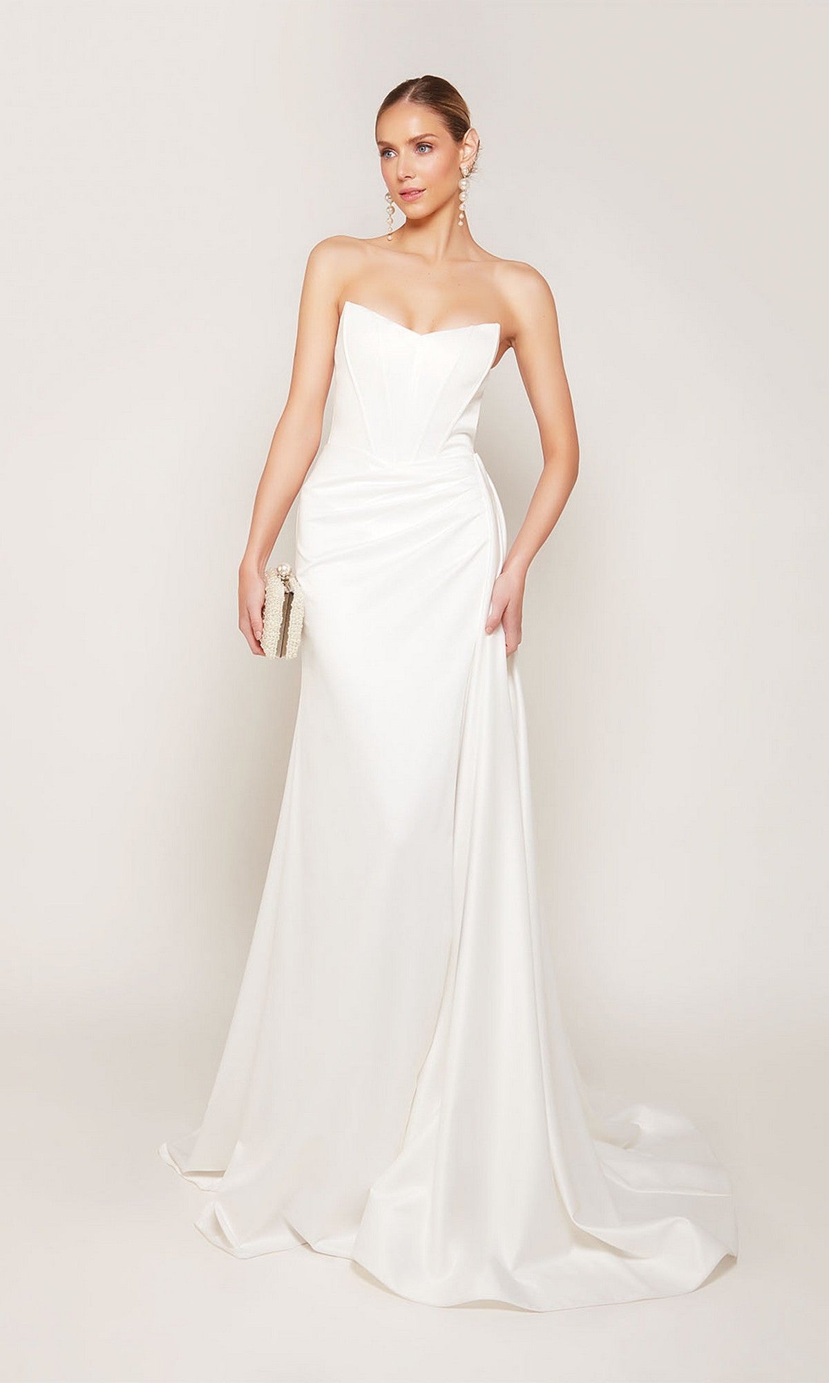 A woman wearing the Alyce 7093 long formal strapless satin dress with a sheath skirt holds a small clutch against a plain light background.